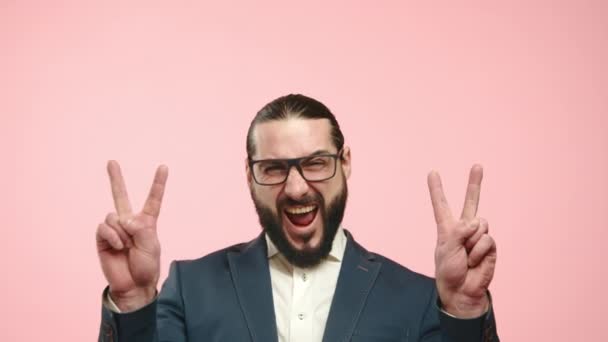 一个衣着华丽 满脸胡须的生意人以和平标志庆祝 他的喜悦在充满活力的粉色背景下是显而易见的 8K照相机 — 图库视频影像
