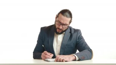 Keskin odaklı bir işadamı titizlikle beyaz bir masaya notlar yazarak profesyonel bir ortamda özveri ve stratejik düşünceyi sembolize ediyor. Kamera 8K HAM. 