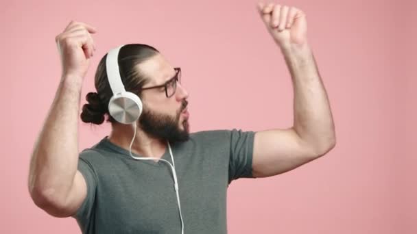 수염과 안경을 남자는 헤드폰을 음악을 즐기고있다 부드러운 분홍색 배경에 행복에 — 비디오