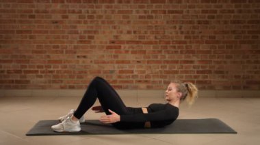 Bir fitness uzmanı topuk dokunuşlarını hassasiyetle yapar, eğik kasları hedef alır ve karın tanımını geliştirir, hepsi tuğla kaplı bir spor salonunun temiz ve yapılandırılmış ortamında.. 