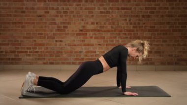 Modern bir fitness stüdyosunda, odaklanmış bir birey diz çökmüş bir tahtayı, çekirdek bağını arttırmak ve yumuşak bir spor paspası üzerinde istikrarı geliştirmek için tasarlanmış bir varyantı icra eder. Kamera 8K HAM. 