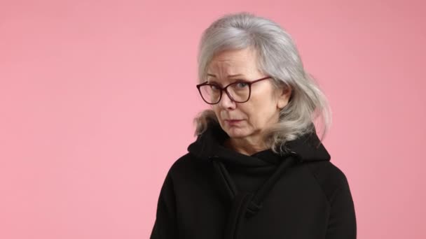 Μια Ηλικιωμένη Γυναίκα Πιασμένη Ένα Απαλό Ροζ Φόντο Κοιτάζει Διακριτικά — Αρχείο Βίντεο