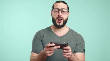 Gözlüklü ve uzun saçlı bir adam olarak yakalanan neşeli bir an, akıllı telefonuyla eğlenceli bir oyun oynarken kahkahaya boğuluyor, saf hazzın bir portresi. Kamera 8K HAM. 