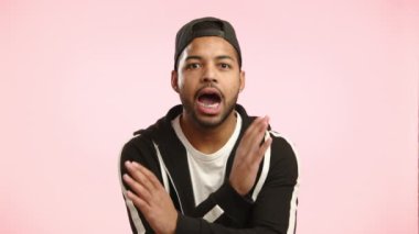 Afro-Amerikalı bir adam elleriyle dur işareti koyuyor. Pembe bir zemine karşı net ve kararlı. Kamera 8K HAM. 