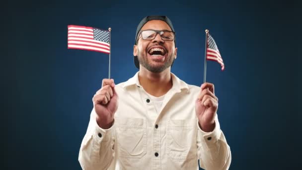 一个快乐的人展示了他的爱国精神 他挥动着美国的两面小国旗 在黑暗 中立的背景下 他快乐的举止闪烁着光芒 8K照相机 — 图库视频影像