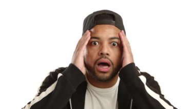 Afro-Amerikalı bir erkeğin tepkisi, beyaz bir arka planda inanılmaz bir sürprizi işlerken geniş gözleri ve elleri kafasının üzerine yerleştirilmiş bir şaşkınlıktır. Kamera 8K HAM. 