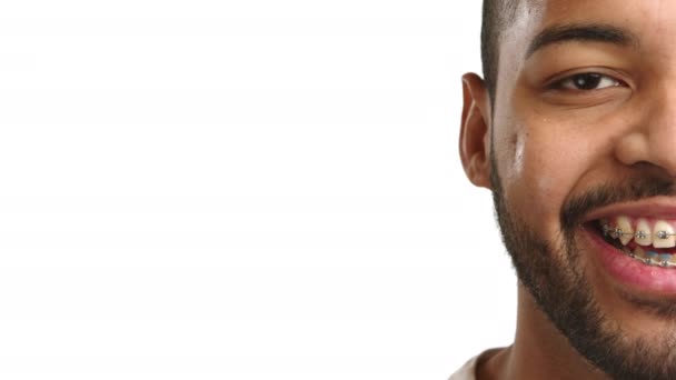 光沢のある歯のブレースを持つ喜ばしいアフリカ系アメリカ人の男性の半面の肖像画は 白い背景に対して明るい笑顔を浮かべています カメラ Raw — ストック動画