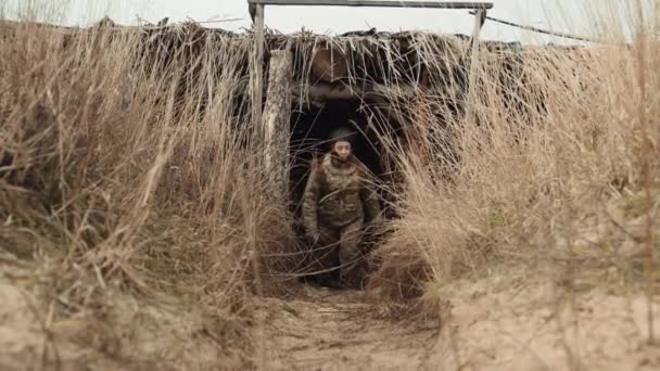 警戒心の強い女性兵士が軍用バンカーから出て行き 完全な戦闘用具で覆われ 彼女の視線は紛争地帯の挑戦的な風景を先に設定しました カメラ Raw — ストック動画