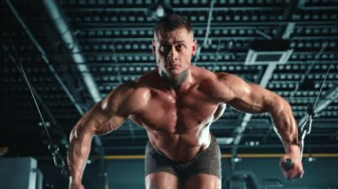 Yoğun odaklı azimli vücut geliştirici, karanlık bir spor salonunda kablo çapraz antrenmanı yapıyor, kaslı fiziğini sergiliyor. Kamera 8K HAM. 