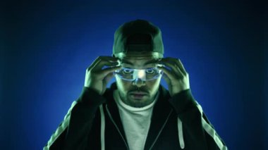 Son teknolojiye dalmış bir adam holografik gözlük takıyor ve canlı mavi bir arka plana karşı gelişmiş dijital yeniliğin bir temsili olan sanal bir klavye ile etkileşime giriyor. Kamera Ham.