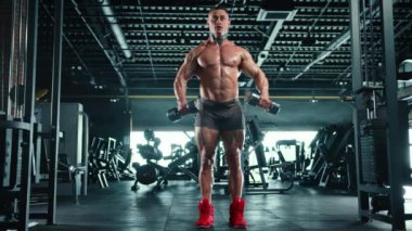Spor salonundaki odaklanmış bir vücut geliştirici, dambıl kaslarını mükemmel formda ve yoğun bir şekilde yükselterek kaslarını geliştirir. Kamera 8K HAM. 