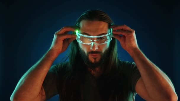 革新的な男性は 周囲の青色光に囲まれたプロジェクトされたキーボードにタイプし始める前に 仮想現実のメガネを調整します カメラ Raw — ストック動画