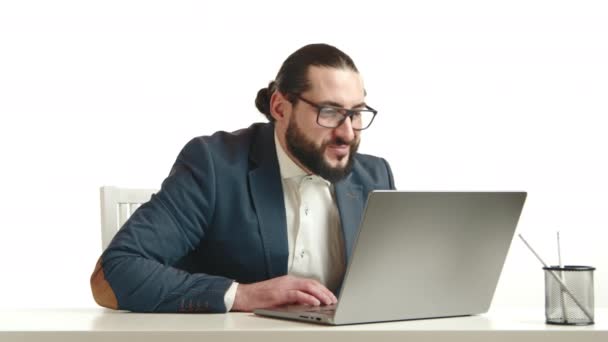 青いジャケットと白いシャツの陽気なひげ付き男は 明るいオフィスの背景に設定されたラップトップ上の活気のあるビデオ通話に従事し 現代の仕事と技術のシームレスなブレンドを反映しています — ストック動画