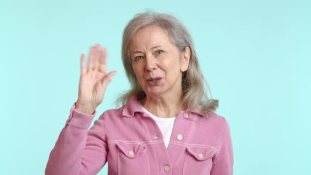 ピンクのジャケットの高齢女性は 心のこもった波に手を伸ばし 彼女の顔は純粋な友情と 柔らかい青い背景に設定された接続したいという欲求を表現しています カメラ Raw — ストック動画