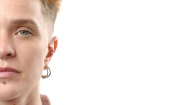 Sanatsal açıdan yakın plan bir fotoğraf genç bir kadının ince detaylarını, yarım yüzünü, piercinglerine vurgu yaparak, titiz beyaz bir arkaplana karşı çekiyor.. 