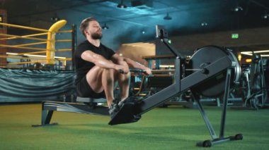 Kendini adamış sakallı bir adam spor salonunda güçlü bir vücut egzersizi yapıyor. Canlı ve dinamik ışıklandırması olan bir spor salonunda kürek çekiyor. Forma olan bağlılığını gösteriyor. Kamera 8K HAM. 
