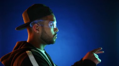 Fütüristik bir deneyime dalmış, şapkalı şık bir adam, önünde yansıtılan sanal klavyeyle etkileşime geçmek için artırılmış gerçeklik gözlüğü kullanıyor, modern teknolojiyi sergiliyor..