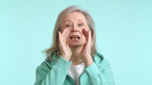 一个活泼的老妇人 双手捂着嘴 大喊着要在周围找到一个人 背靠着平静的蓝色背景 8K照相机 — 图库视频影像