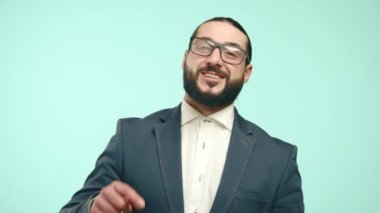 Takım elbiseli sakallı bir adam, hafif bir turkuaz arka plana karşı beğenileri ve takipçileri cesaretlendiriyor. Promosyon ve reklam malzemesi için ideal. Kamera 8K HAM. 