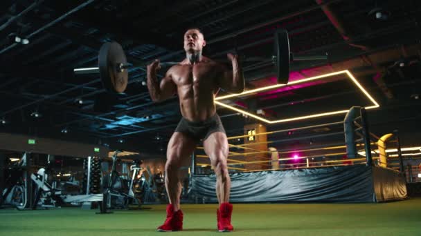 一位强壮的男性健美运动员 拥有令人印象深刻的肌肉 在一个配备先进设备的当代健身中心做杠铃式蹲 表现出力量和耐力 8K照相机 — 图库视频影像