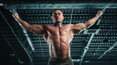 Kas geliştiren vücut geliştirici çapraz kablo makinesinde pazı egzersizi yapıyor, bir spor salonunda güç ve bağlılık gösteriyor. Kamera 8K HAM. 