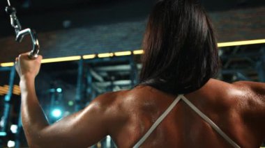 Çapraz makinede egzersiz yapan bir bayan sporcunun yakın plan çekimi, modern bir spor salonunda yaptığı egzersizin yoğunluğunu ön plana çıkarıyor. Kamera 8K HAM. 