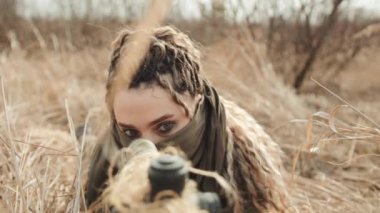 Keskin nişancı bir kadın tüfeğinin optik dürbününden bakarken kameranın odaklanmış yüzünden keskin nişancı tüfeğinin namlusuna doğru döndüğü görülüyor. Kamera 8K HAM. 