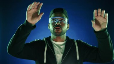 Yoğunlaşmış genç bir adam, sanal bir arayüzle etkileşime geçmek için artırılmış gerçeklik gözlüğü takan, yüksek teknolojili bir deneyime dalmış, görünmeyen dijital dünyaya karşı manipüle edilmiş eller 