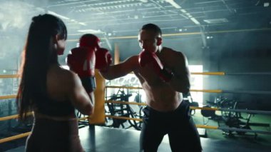 Bir erkek ve kadın boksör birlikte antrenman yapar, yumruklaşır ve iyi aydınlatılmış bir spor salonunda savunma teknikleri uygular, boks yeteneklerini geliştirir. Kamera 8K HAM. 