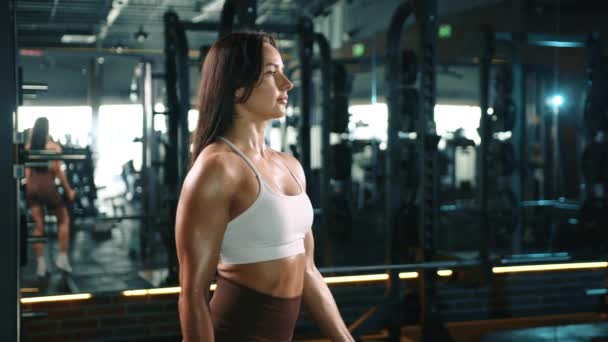 ダンベルで二重カールを実行する焦点を当てた女性のフィットネスコーチは 設備の整ったジムでの筋肉の発達と強化への献身を例示します カメラ Raw — ストック動画