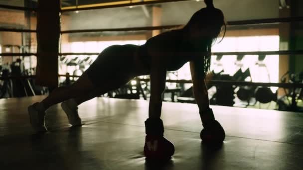 一个戴拳击手套的女拳击手主要通过在拳击台的垫子上俯卧撑 展示奉献和运动形式来增加她的核心和上身力量 8K照相机 — 图库视频影像