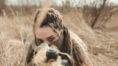 Keskin nişancı bir kadın tüfeğinin optik dürbününden bakarken kameranın odaklanmış yüzünden keskin nişancı tüfeğinin namlusuna doğru döndüğü görülüyor. Kamera 8K HAM. 