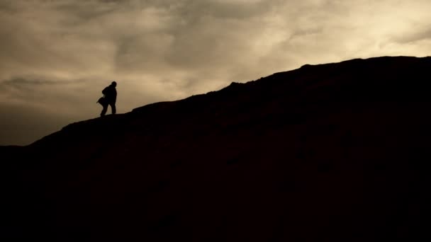 兵士の孤独な姿が夕暮れに丘の上に登り 彼らのシルエットは暗くなる空に向かってエッチングされ 彼らの使命の重力を捉える劇的なフレームです カメラ Raw — ストック動画