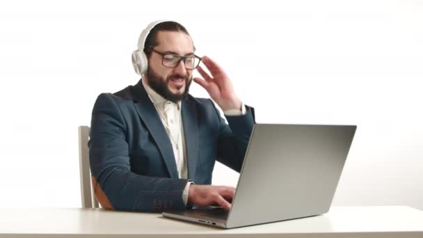 一位有着长长的深色胡须和眼镜的快乐的商人在工作中找到了乐趣 一边用耳机一边用笔记本电脑 这清楚地表明了现代工作的灵活性和满足感 — 图库视频影像