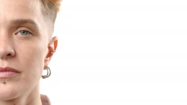 Sanatsal açıdan yakın plan bir fotoğraf genç bir kadının ince detaylarını, yarım yüzünü, piercinglerine vurgu yaparak, titiz beyaz bir arkaplana karşı çekiyor.. 