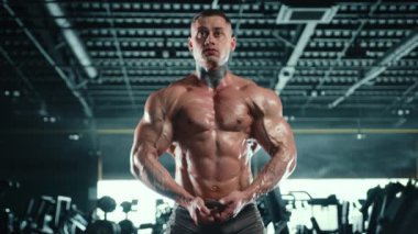 İyi yapılı bir vücut geliştirici spor salonunda güçlü poz verir. Dalgalanan kasları vücut geliştirmek için saatlerce kendini adamış ve çok çalışmıştır. Kamera 8K HAM. 