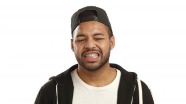 Diş telleri olan Afro-Amerikalı bir adam utangaç ve biraz utangaç görünür, eli ağzını kapatır, utangaçlık ya da beyaz bir arka planda dil sürçmesi hissi verir. Kamera Ham.