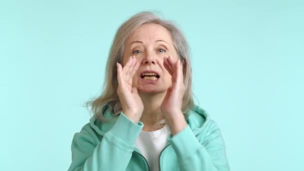 一个活泼的老妇人 双手捂着嘴 大喊着要在周围找到一个人 背靠着平静的蓝色背景 8K照相机 — 图库视频影像