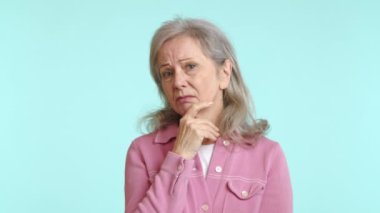 Düşünceli, kasvetli bir ifadeye sahip son sınıf öğrencisi bir kadın derin düşüncelere dalmış, parmağı çenesinde yansımayı ve düşünmeyi sembolize ediyor, pastel renkli bir arka planda. Kamera 8K HAM. 