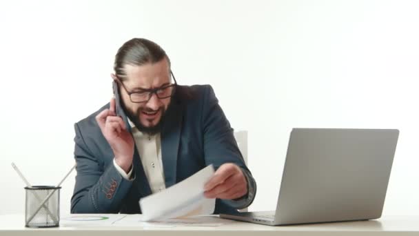 メガネと青いスーツと白いシャツのひげを持つ皮肉なビジネスマンは 不安定な財務文書を見ながら電話で熱い会話をしています カメラ Raw — ストック動画