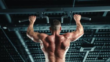 Üst vücut gücüne odaklanan kaslı sırt kaslı bir adam son model bir fitness merkezinde yatay bir çubuğa tutunuyor. Kamera 8K HAM. 