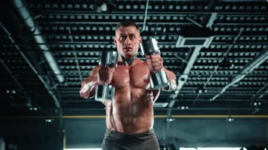 Terli, kaslı bir adam spor salonunda yüksek kontrastlı ışıklandırmayla ağır dambılları rahatça kaldırır. Onun yoğun bakışları ve fiziği güç yayıyor. Kamera 8K HAM. 