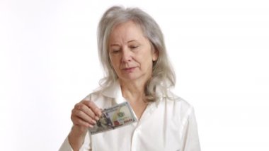 Düşünceli bir ifadeye sahip olgun bir bayan beyaz bir arka planda finansal kararları ya da kaybı sembolize eden yüz dolarlık banknotu kesinlikle ikiye böler. Kamera 8K HAM. 