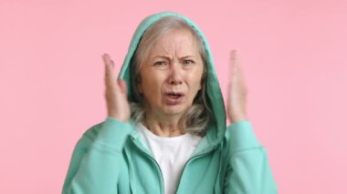 Sıkıntılı yaşlı bir kadın elleriyle kulaklarını kapatıyor, soluk pembe bir arka plana karşı çok gürültülü ve rahatsız edici bir sese karşı sorunlu bir tepki gösteriyor. Kamera 8K HAM. 