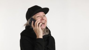 Siyah şapkalı mutlu bir kadın, bir telefon konuşmasında, kolları kapalı bir şekilde el kol hareketleriyle meşgul..