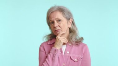 Düşünceli, kasvetli bir ifadeye sahip son sınıf öğrencisi bir kadın derin düşüncelere dalmış, parmağı çenesinde yansımayı ve düşünmeyi sembolize ediyor, pastel renkli bir arka planda. Kamera 8K HAM. 