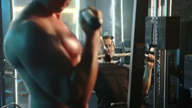 Spor salonlarına dalmış iki adam, spor aletleriyle çevrili güç antrenmanlarına katılırken bağlılıklarını ve konsantrasyonlarını sergiliyorlar. Kamera 8K HAM. 