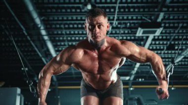 Yoğun odaklı azimli vücut geliştirici, karanlık bir spor salonunda kablo çapraz antrenmanı yapıyor, kaslı fiziğini sergiliyor. Kamera 8K HAM. 