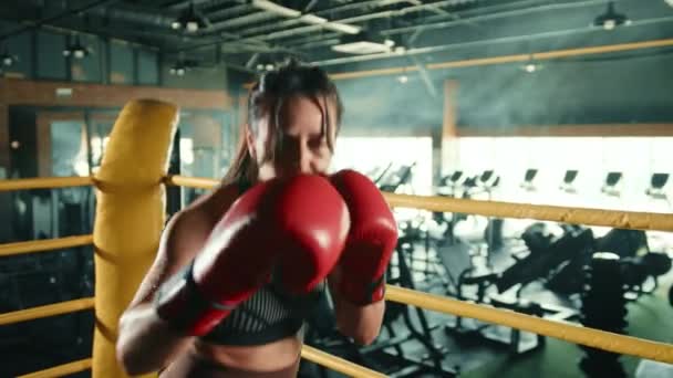 赤い手袋に焦点を当てた女性ボクサーは 都市ジムのボクシングバッグで精力的にトレーニングを行い すべてのパンチで彼女の決意と強さを示しています カメラ Raw — ストック動画