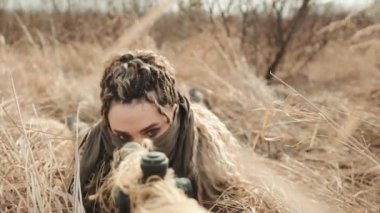 Keskin nişancı, uzun otların arasına saklanmış, tüfeğin dürbününe odaklanmış, ıssız bir alana kurulmuş. Askeri operasyonlarda taktik, hassasiyet ve sabır. Kamera 8K HAM. 